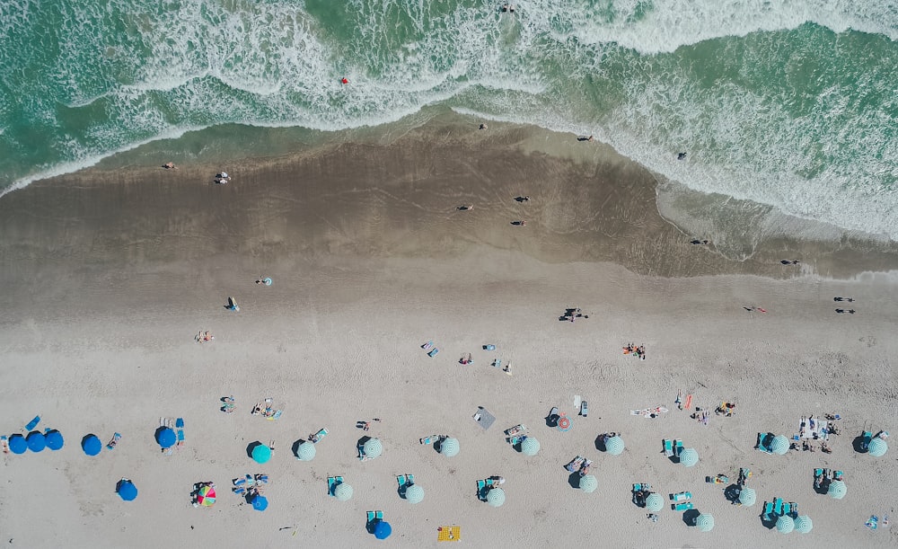 An aerial shot of vacationers on a sandy beach with blue umbrellas and deck chairs