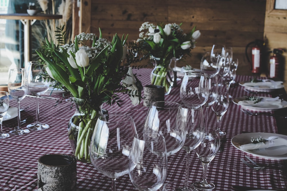 verres à vin transparents à côté de la pièce maîtresse fleur blanche sur une couverture de table rouge et blanche