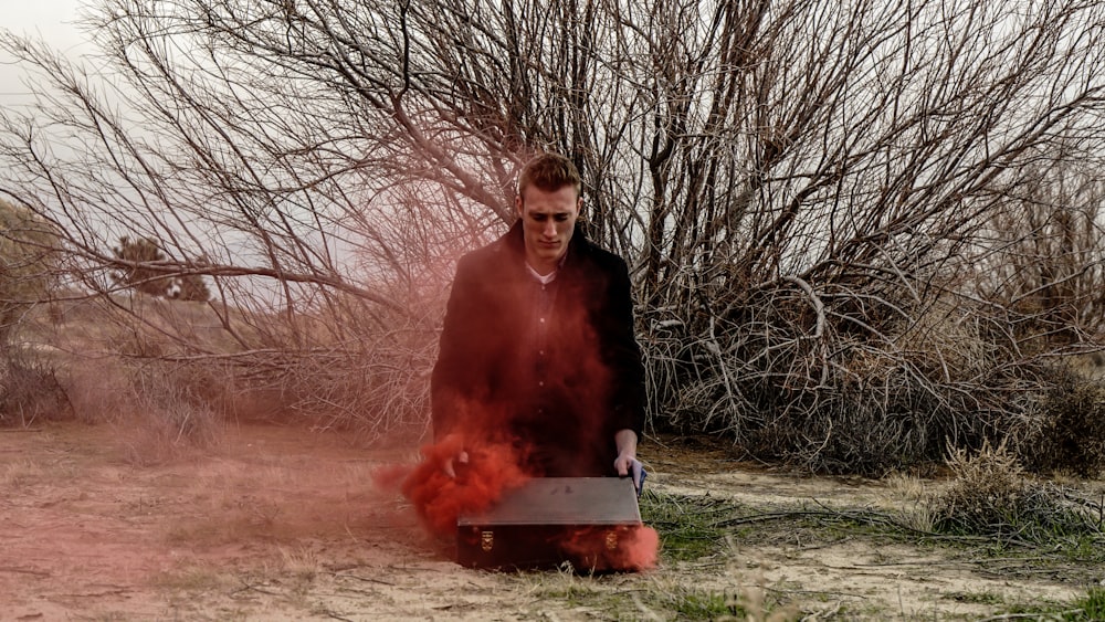 A man opening his suitcase on the ground, as red smoke escapes it.