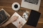 person holding ballpoint pen writing on notebook