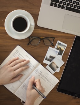 person holding ballpoint pen writing on notebook