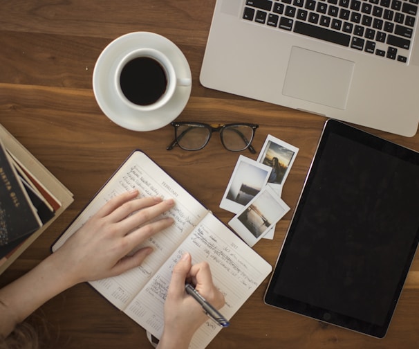 person holding ballpoint pen writing on notebook