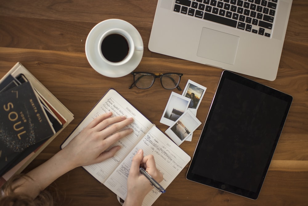 An overhead short of a woman writing in a journal at a busy table with a cup of coffee