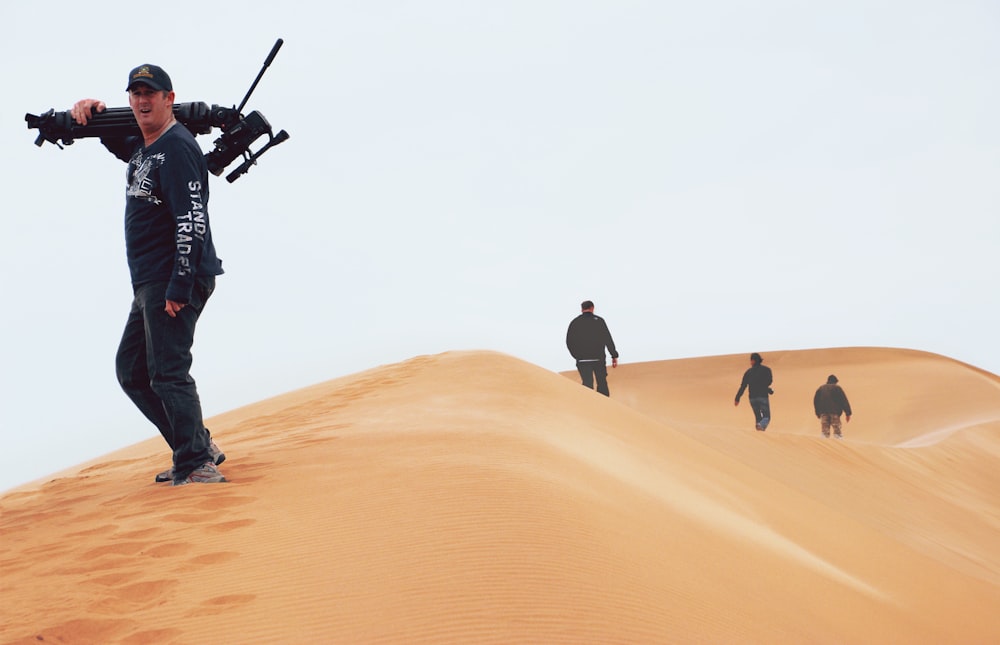 man in black jacket and pants holding black and gray stick on brown sand