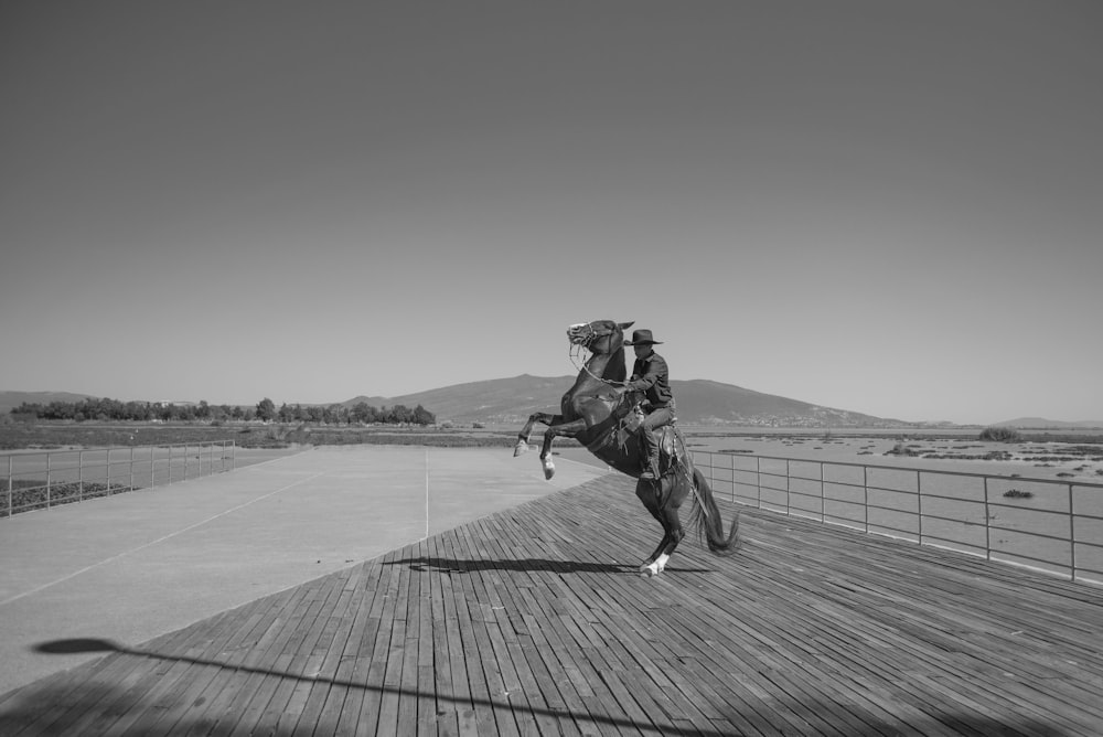 Graustufenfoto eines Mannes in Jacke und Hose, der auf einem Pferd reitet