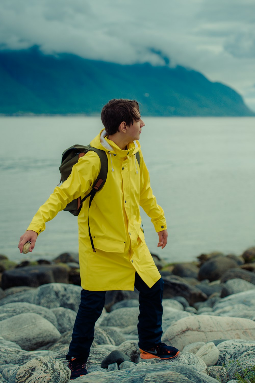 boy in yellow jacket standing on rock near body of water during daytime