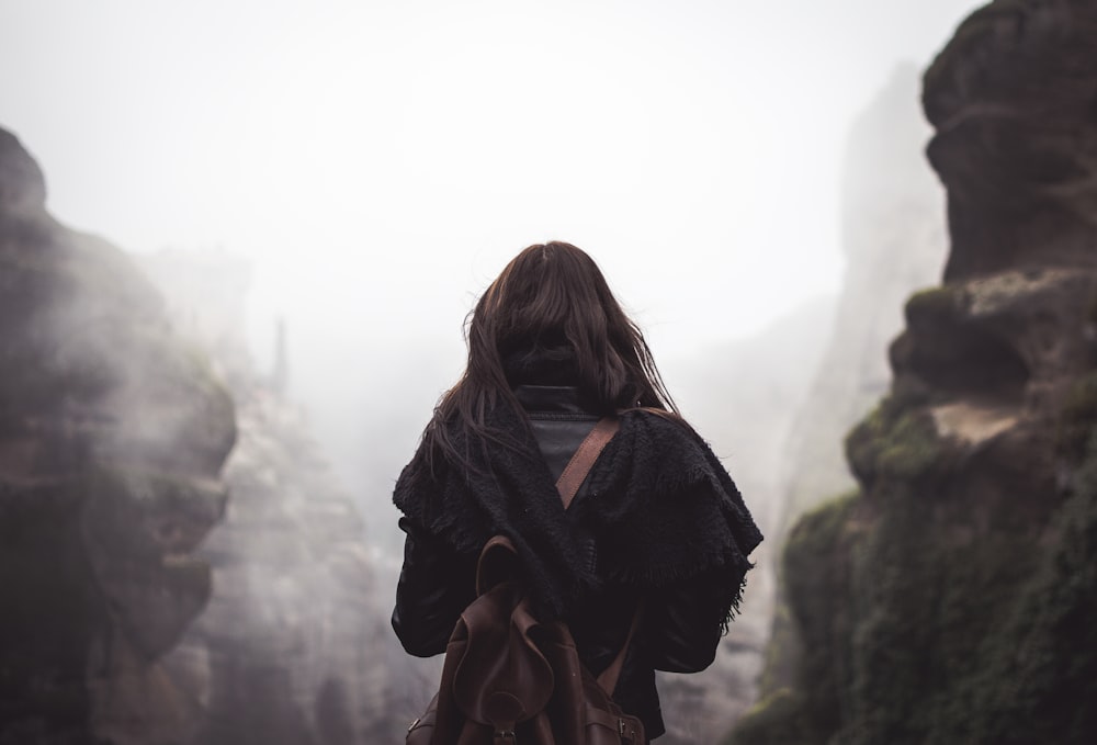 昼間、山の前に立つ茶色のリュックサックを背負った女性