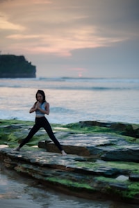 woman doing yoga on rock platform next to body of water