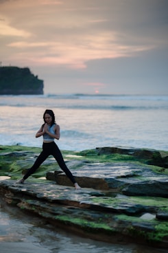 woman doing yoga on rock platform next to body of water
