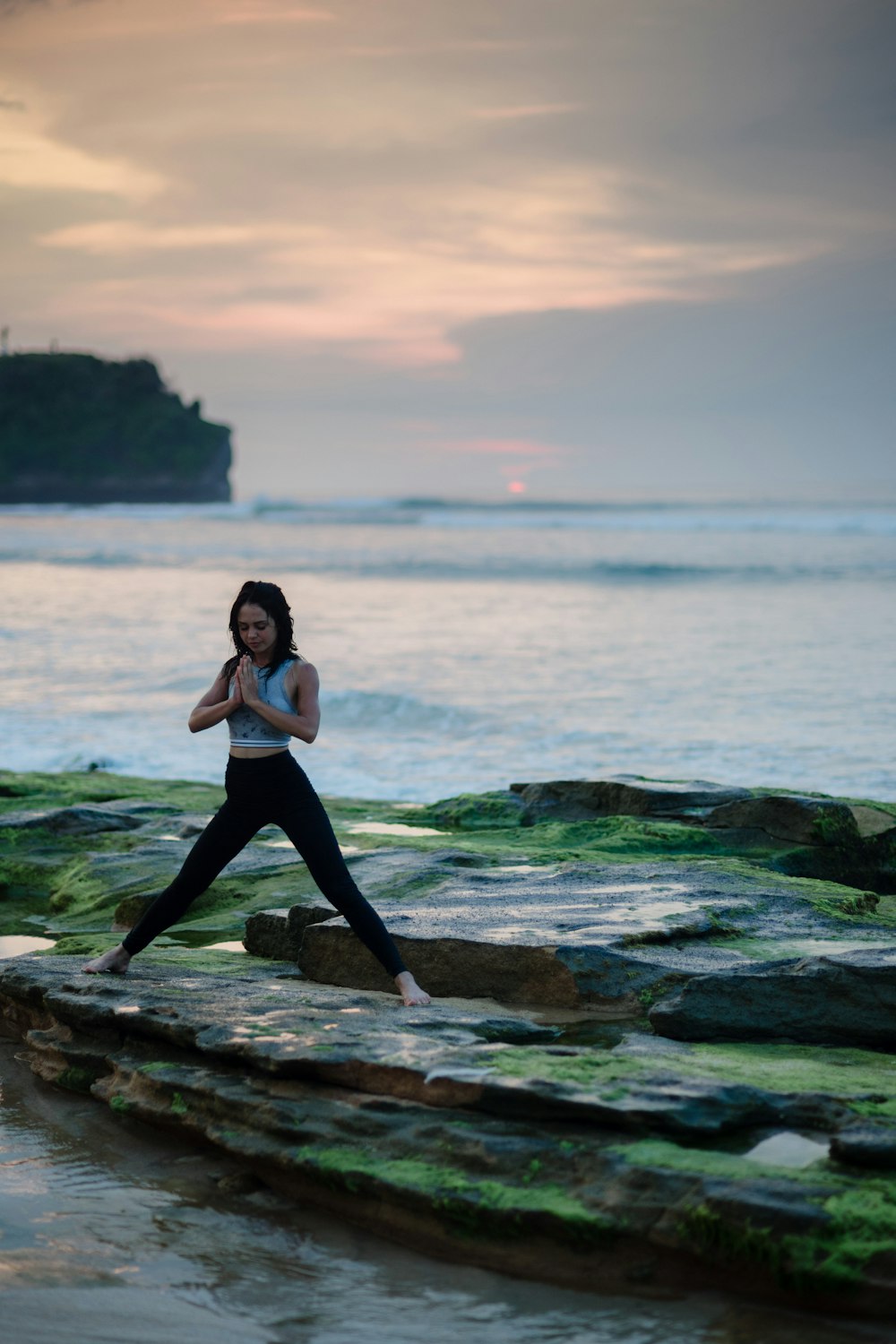 Mujer haciendo yoga en la plataforma de roca junto al cuerpo de agua