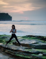 woman doing yoga on rock platform next to body of water