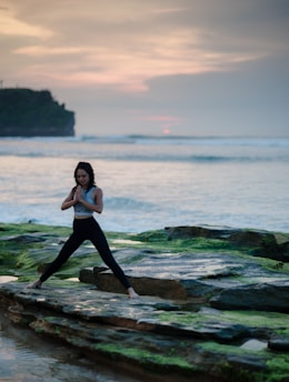 woman doing yoga on rock platform next to body of water