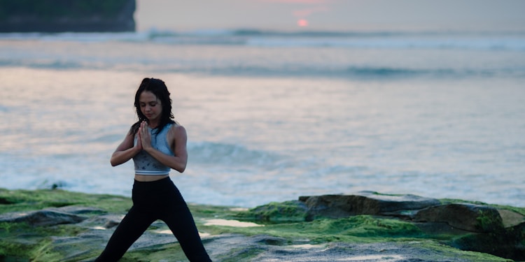 woman doing yoga on rock platform next to body of water