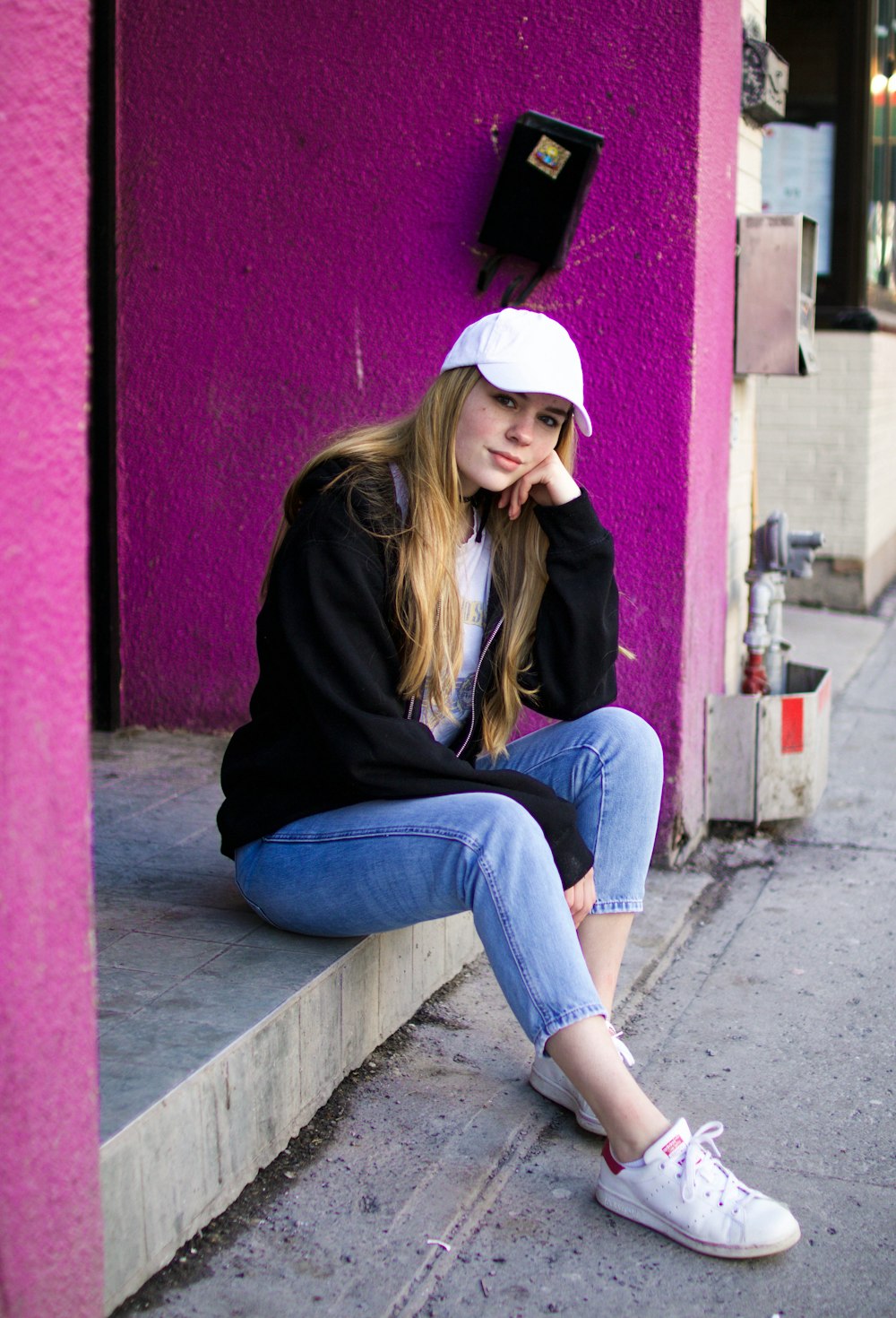 Frau in schwarzer Jacke und blauer Jeans sitzt im Freien