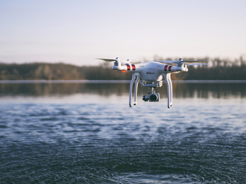 Dron cuadricóptero blanco volando sobre el cuerpo de agua