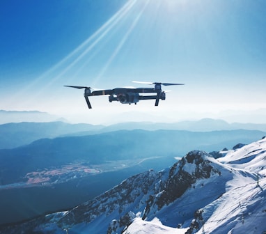 white quadcopter drone flying near snow mountain during daytime