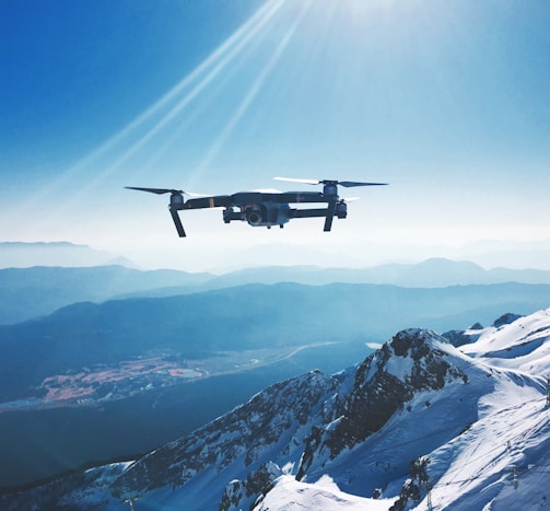 white quadcopter drone flying near snow mountain during daytime