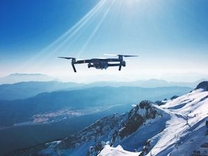 white quadcopter drone flying near snow mountain during daytime