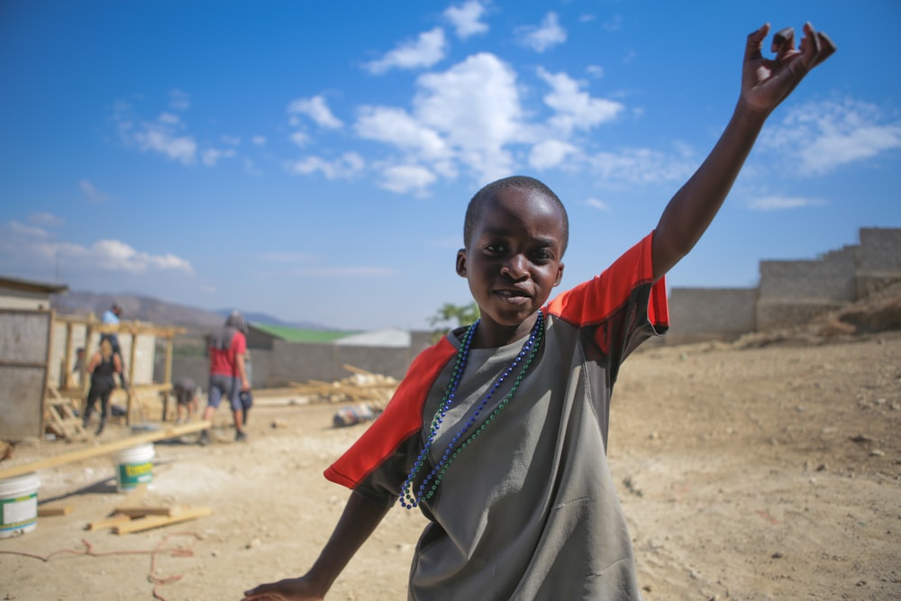 boy wear gray and orange shirt standing while raising his left hand