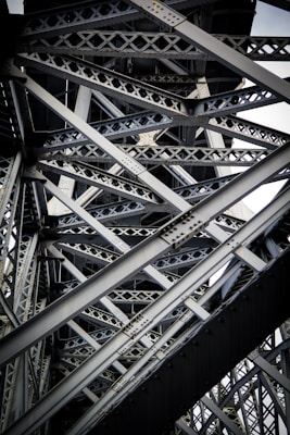Intricate steel beams and trusses form a complex lattice structure, showcasing industrial design and engineering. The interlocking metal components create geometric patterns with rivets visible throughout the structure.