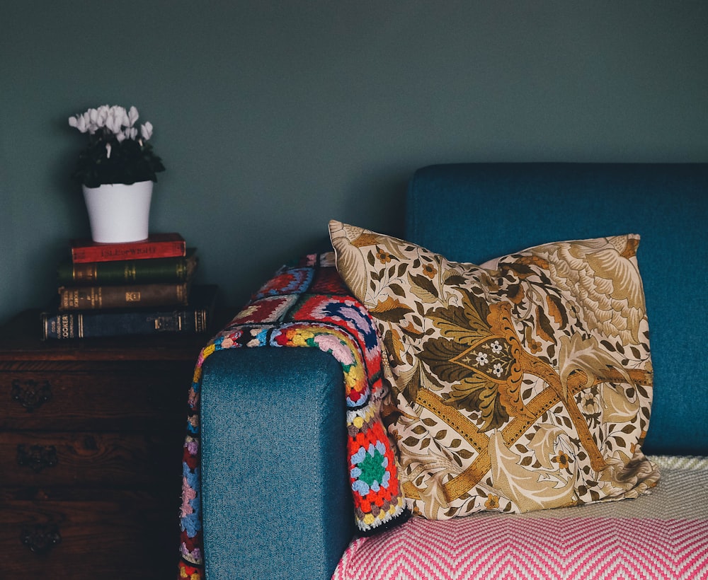 yellow throw pillow on blue couch beside on pile of books on top of drawer