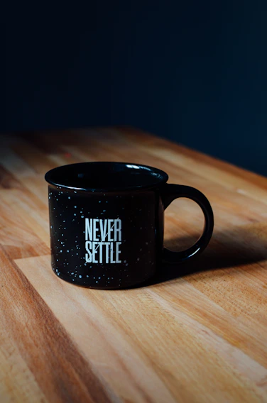 A close-up of a white mug with a bold black quote about rent stress, sitting on a minimalist wooden table.