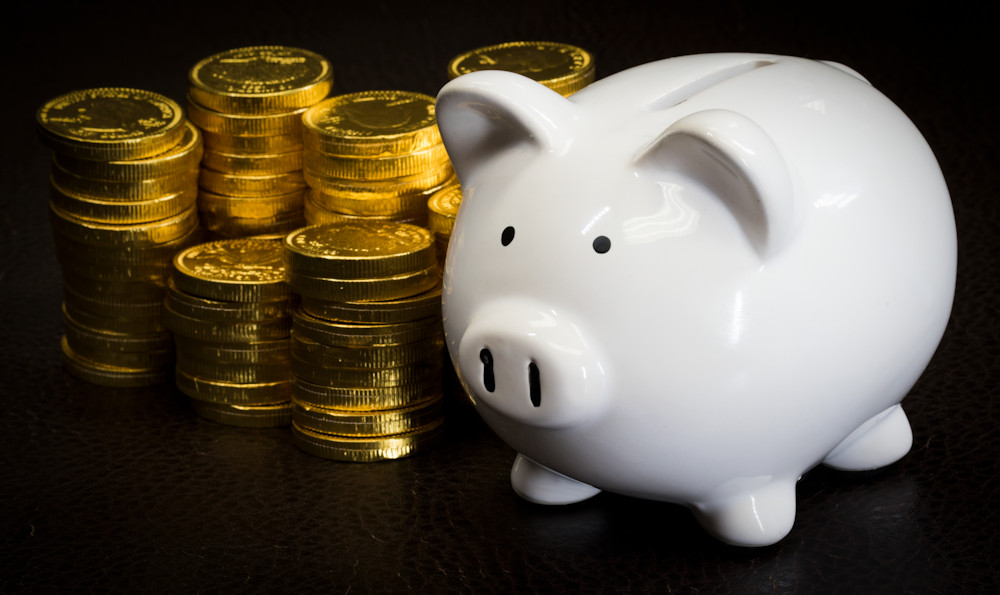 A white piggy bank next to a bunch of stacked gold coins.