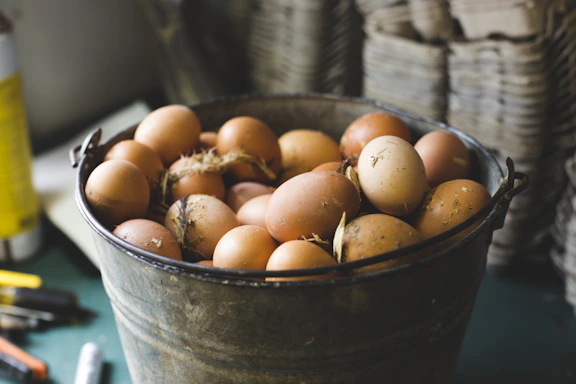 A rustic wooden crate filled with fresh brown and white eggs sitting on a farmhouse table.
