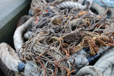 A tangled mass of various ropes and nets with different textures and hues, predominantly in earthy tones, is piled together. The ropes appear weathered and worn, suggesting heavy use.