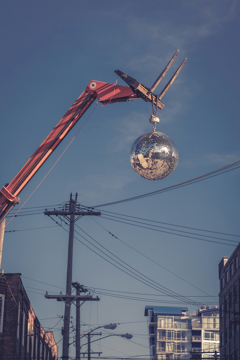 worm's-eye view photography of red and silver wrecking ball near electric post under clear blue sky