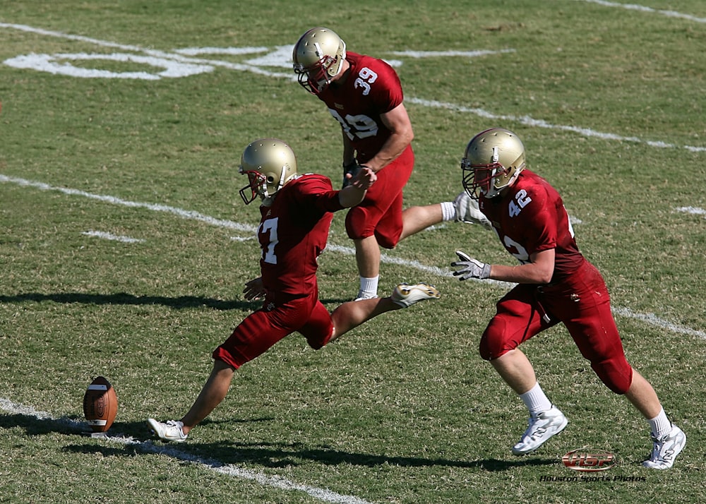 three football players running towards football ball at field during daytime