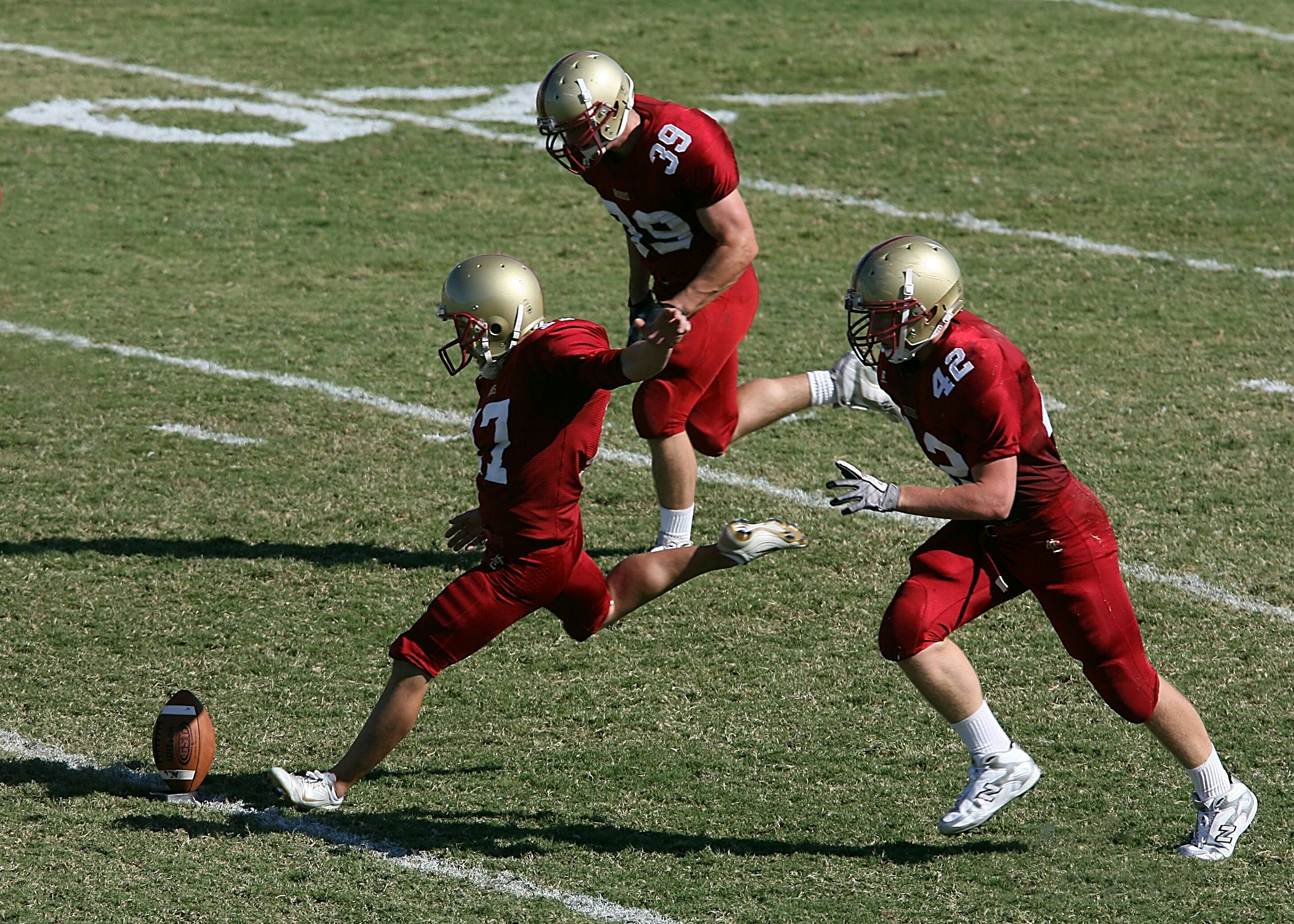College player prepares to kick the ball to start the game.  His teammates prepare to accompany him downfield.