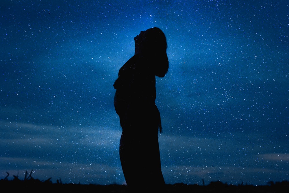a silhouette of a person standing under a night sky