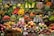 A vibrant market display filled with an assortment of fruits and vegetables, including apples, oranges, asparagus, eggplants, pumpkins, pineapples, and leafy greens. The produce is neatly organized and labeled, showcasing a variety of colors and textures.