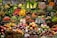A vibrant market display filled with an assortment of fruits and vegetables, including apples, oranges, asparagus, eggplants, pumpkins, pineapples, and leafy greens. The produce is neatly organized and labeled, showcasing a variety of colors and textures.