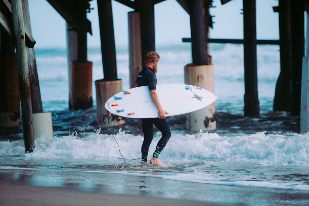 homme tenant une planche de surf blanche