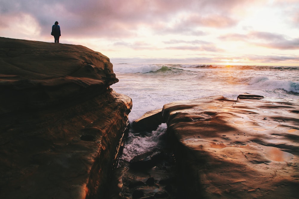 person standing on a cliff facing body of water