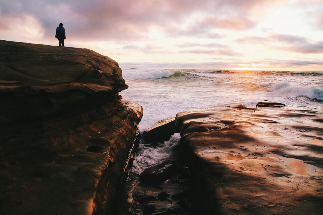 person standing on a cliff facing body of water