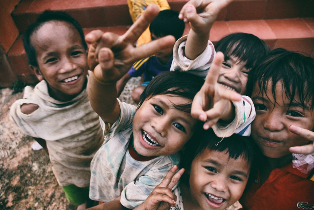 Cinco niños sonriendo mientras hacen la señal de la paz con la mano