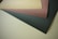 Four overlapping sheets of paper in different colors lie flat on a surface. The paper colors include light brown, dark brown, beige, and black.