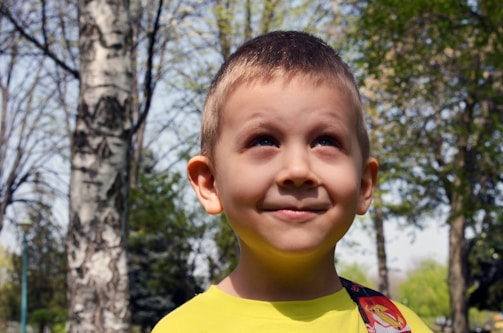 A child smiling while listening to a story being read aloud in a sunny park.