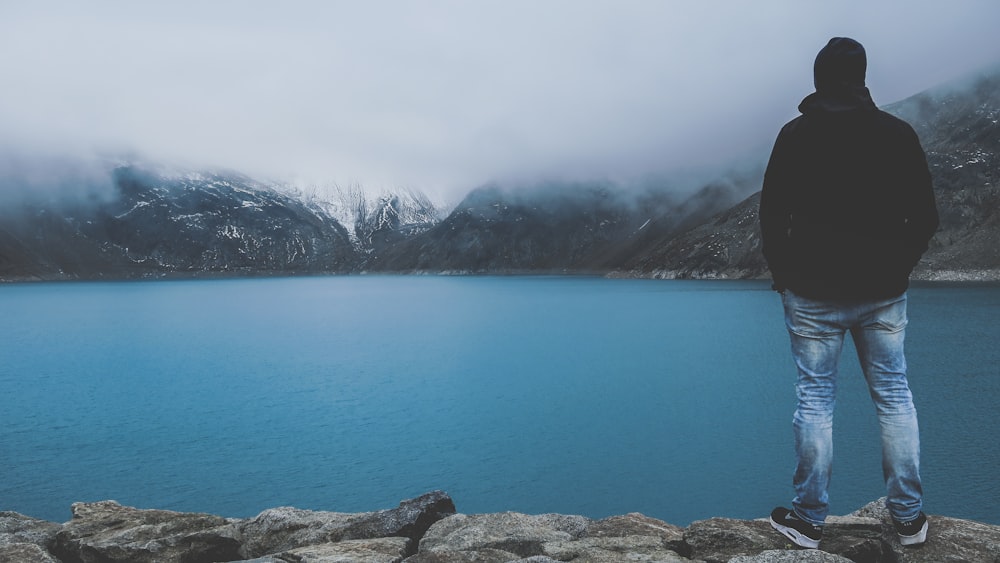 man standing on cliff facing bod of water