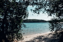 A serene beach scene with lush greenery framing white sands and clear blue sea at dawn.