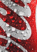 Close-up of a red and silver aluminum can featuring water droplets on its surface, creating a refreshing and cool appearance.