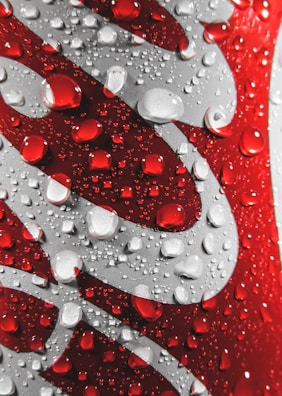 Close-up of a red and silver aluminum can featuring water droplets on its surface, creating a refreshing and cool appearance.