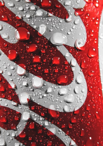 Close-up of a red and silver aluminum can featuring water droplets on its surface, creating a refreshing and cool appearance.