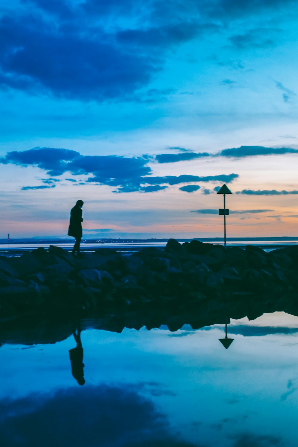 silhouette of person walking on rocks near body of water