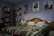 A dog lies comfortably on a neatly made bed, which has a colorful patterned blanket and pillows. Bookshelves filled with books line the walls, and several posters are displayed above the bed. The room is softly lit, creating a cozy atmosphere.
