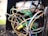 A chaotic tangle of multicolored electrical wires, including green, blue, black, and yellow, in what appears to be an electrical box. Some wires are frayed or damaged, and there is a yellow wire connector in the mix. The scene suggests neglect or disrepair.