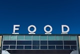 Large white letters spelling 'FOOD' are prominently displayed atop a building against a clear blue sky. The building facade features multiple rectangular windows with a modern design.